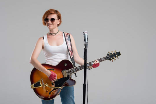 Portrait of a beautiful young rock woman in sunglasses with a guitar. She sings a song in studio microphone