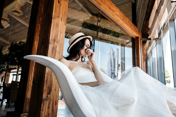 Obraz na płótnie Canvas Portrait of beautiful smiling bride wearing straw hat and stylish white dress at wedding day
