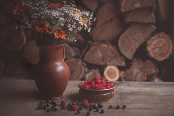 Fresh berries of raspberries and currants on the table near a bouquet of flowers. Rural atmosphere. Comfort. 