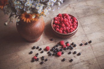 Fresh berries of raspberries and currants on the table near a bouquet of flowers. Rural atmosphere. Comfort. 