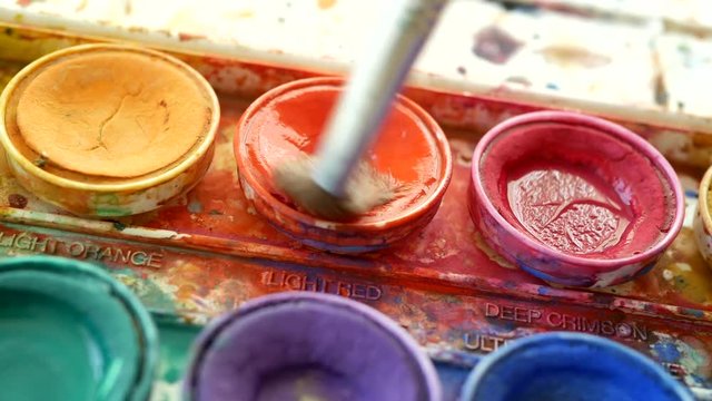 Artists watercolor palette messy with yellow, orange, red and purple paint