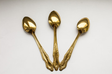 Three little golden teaspoons on white background