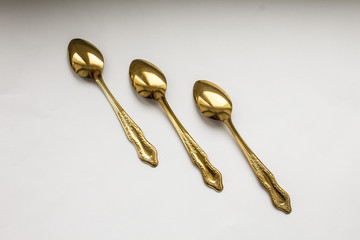 Three small golden teaspoons on white background