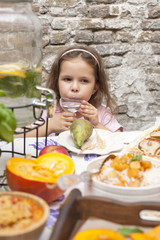 A little girl at a dinner table in the courtyard of the house. Delicious family dinner with autumn foods and fruits. Copy space,