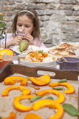 A little girl at a dinner table in the courtyard of the house. Delicious family dinner with autumn foods and fruits. Copy space.