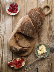 Homemade sliced rye bread on a wooden table and a sandwich with butter and jam.