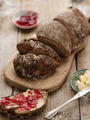 Homemade sliced rye bread on a wooden table and a sandwich with butter and jam.