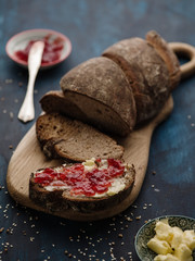 Homemade sliced rye bread on a wooden table and a sandwich with butter and jam.