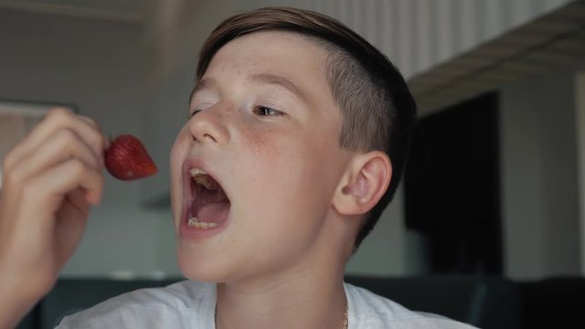 Smiling boy at breakfast eating fruit cherries and strawberries