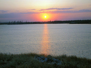 Fototapeta premium The sunset sky over the sea, against a blurred, industrial landscape.