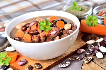 Bean soup with large beans on cutting board, carrots, parsley, marjoram, spoon and ladle