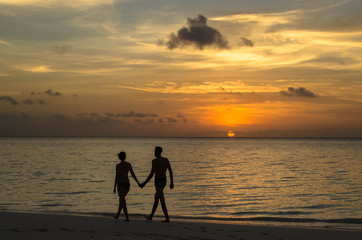 A couple is holding hands and walking at the beach during the sunset. Golden hour of the sunset.