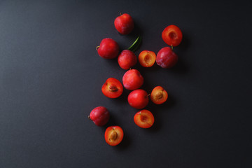 Red sweet cherry plums on dark background, whole and halved. Overhead view