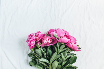 Flat lay, top view of pink peonies flower bouquet on white blanket background. Minimal summer floral concept.