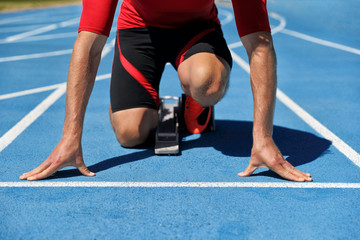 Runner athlete starting running at start of run track on blue running tracks at outdoor athletics and fiel stadium. Sport and fitness man lower body, legs and running shoes going sprinting.