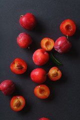 Red sweet cherry plums on dark background, whole and halved. Overhead view