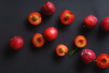 Red sweet cherry plums on dark background, whole and halved. Overhead view
