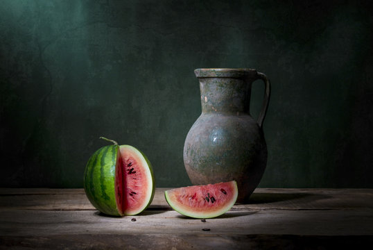 still life with one small whole green watermelon, two peers, a jug and a bunch of ears and poppy seed heads. Art photography.