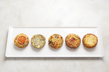 Five individual quiche pies on a white rectangular plate