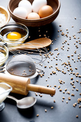 Baking ingredients. Bowl, eggs, flour, eggbeater, rolling pin and eggshells on black chalkboard from above.