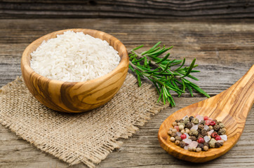 Rice in bowl and spoon with condiments next.  Long rice. Uncooked rice in a wooden bowl