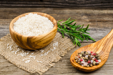 Rice in bowl and spoon with condiments next.  Long rice. Uncooked rice in a wooden bowl