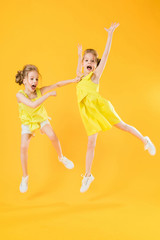 The girls of the twins are dancing together on a yellow background.