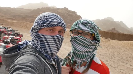 Two happy married couple bikers near atvs quad bike in sand desert nature. All terrain vehicle in desert on rocky mountains background. Off road driving on desert road