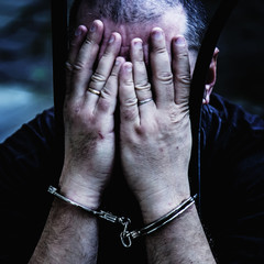 Portrait of handcuffed criminal man imprisoned. Arrest, gangster, pain concept.