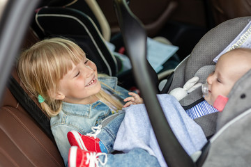 Brother and sister sitting in car in safety seat. Siblings on passenger places having fun together during travel by vehicle. Travelling with children concept