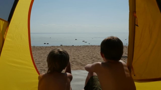 Rear view of two boys sitting inside the tent and admiring the sea
