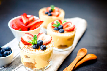 homemade, exquisite dessert tiramisu in glasses decorated with strawberry, blueberry, mint on black wooden table