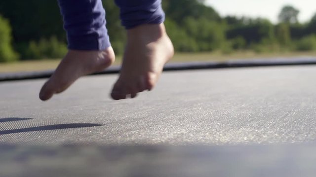Slow-motion of the feet of a girl / child jumping on a trampoline. With sunflare at Sunset / Sunrise.