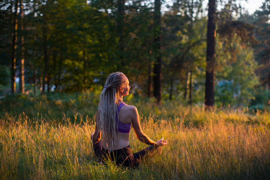 Woman yoga with long hair dreadlocks meditates on nature.