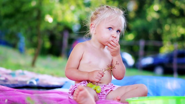 Little girl eating fresh grapes and lookind at the camera. Cute kid Eats Fruits outdoors.