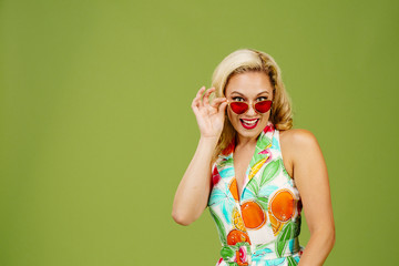 Flirty blonde woman peeking from under her red sunglasses, isolated on green studio background