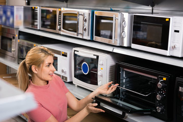 Fototapeta na wymiar Positive female looking new microwave for kitchen in furniture store