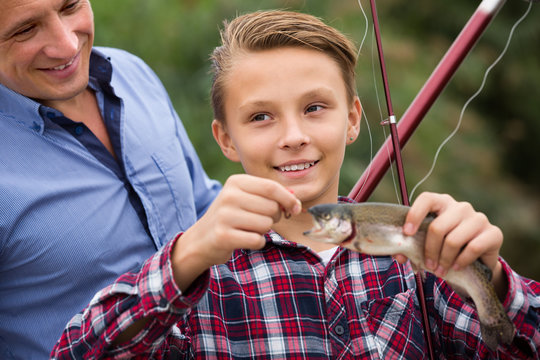 Happy man with son looking at fish on hook