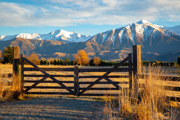 A closed wooden farm gate at the entrance to a farm in the high country below snowy mountains