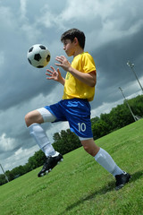 Active child soccer player bouncing (juggling) ball off his thigh