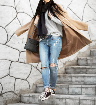 All fashion outfit details. Fashionable woman wearing coat, ripped jeans with sneakers.