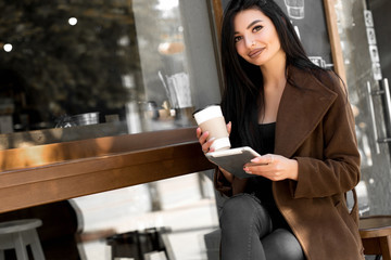 Beautiful girl uses a tablet and drinks coffee, sitting in a cozy cafe.