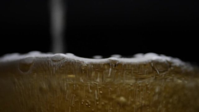 Beer is pouring into glass with foam sliding down side of beer glass