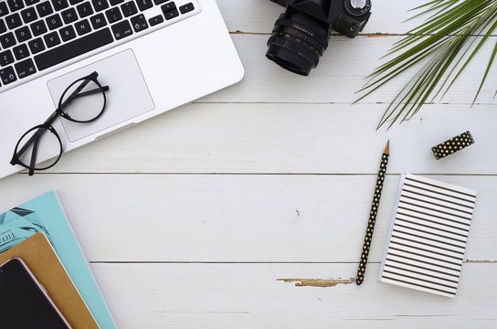 Frame made of laptop, eyeglasses, palm leaf and notebook on white wooden background. Flat lay business mockup. Freelancer workspace.