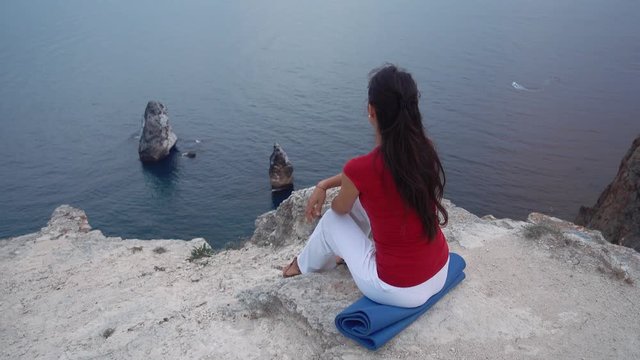 girl sitting on rock by sea, meditating in lotus yoga pose, concentrating, relaxing mind, soul and body.
