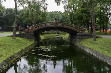 Fototapeta na wymiar Curve bridge in the park cross small pond
