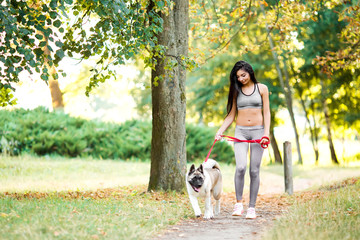 Naklejka na ściany i meble Sports woman walking with dog in the park.
