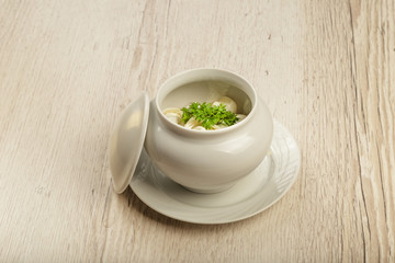 Dumplings in a white pot with sour cream and greens on a wooden background.
