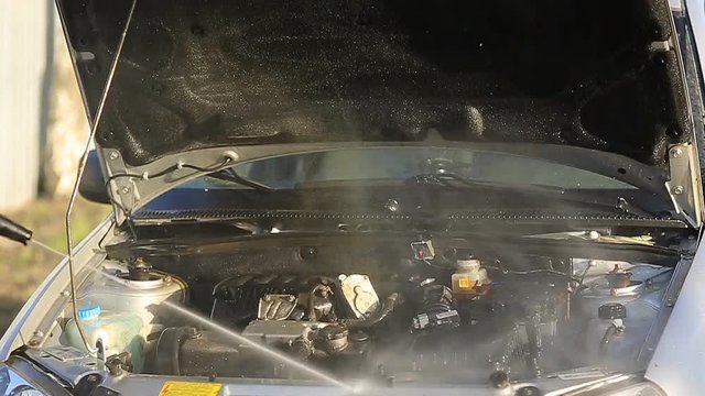 Young attractive man perfusing with water his silver car