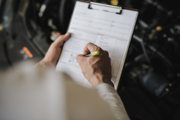Hand of young man mechanic holding clipboard checklist the car at service center repair